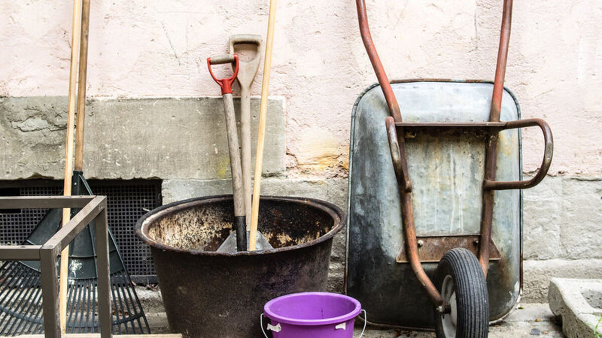 Well-used garden tools, wheelbarrow and bucket lined up against a wall