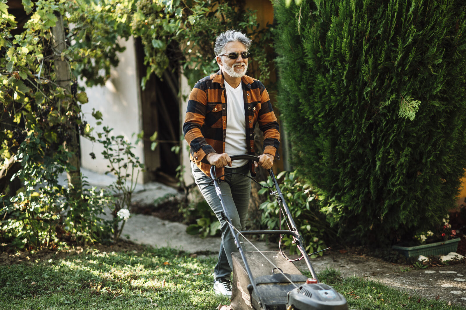 Gardener pushing a petrol mower through a sunny backyard garden
