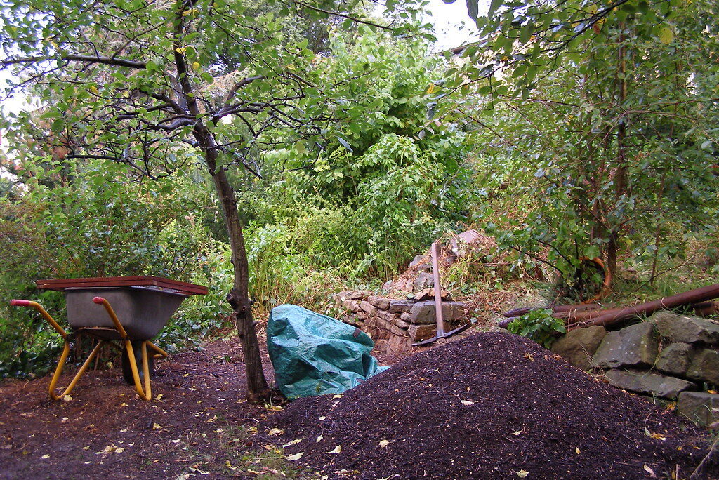 Mulch pile, spade and wheelbarrow at work in a garden clearance